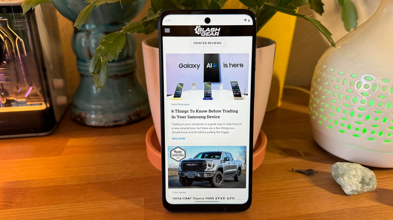 Motorola G Play (2024) on the MMtech Online website on a wooden table resting against some potted plants.