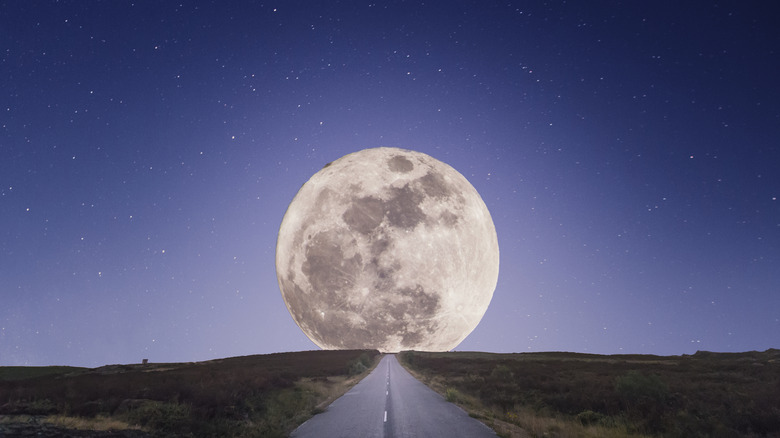 A visual of the moon in the sky before a road.