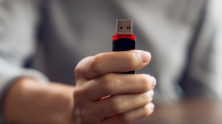 A person holding up a USB flash drive.