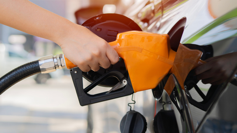 A woman's hand holding an orange gas pump nozzle fueling up her vehicle