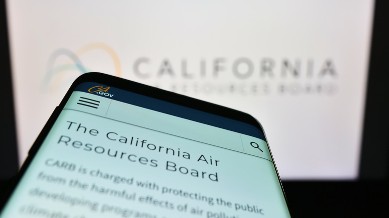 A close-up of a cell phone with the California Air Resources Board website displayed with the logo in white blurred in the background
