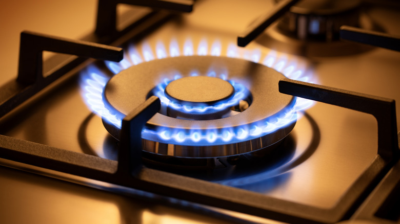 A burner lit on a standard gas stove, orange lighting
