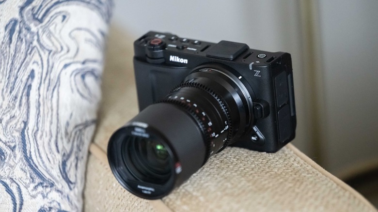The Nikon Zr sitting on top of a couch cushion with a lens attached.