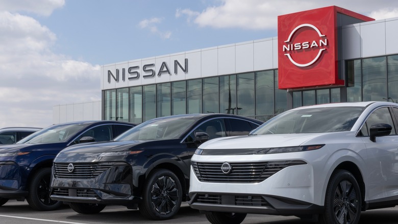 Three Nissan car models parked in front of a Nissan dealership.