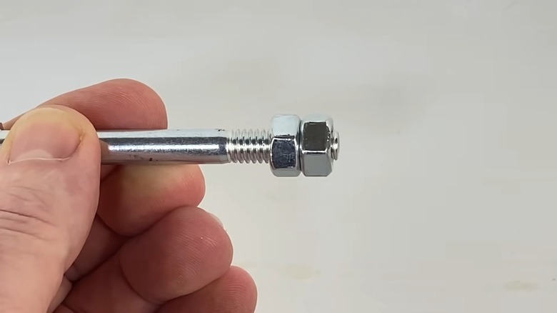 A Hand Holding A Bolt With Two Nuts Tightened Together As An Allen Wrench Alternative