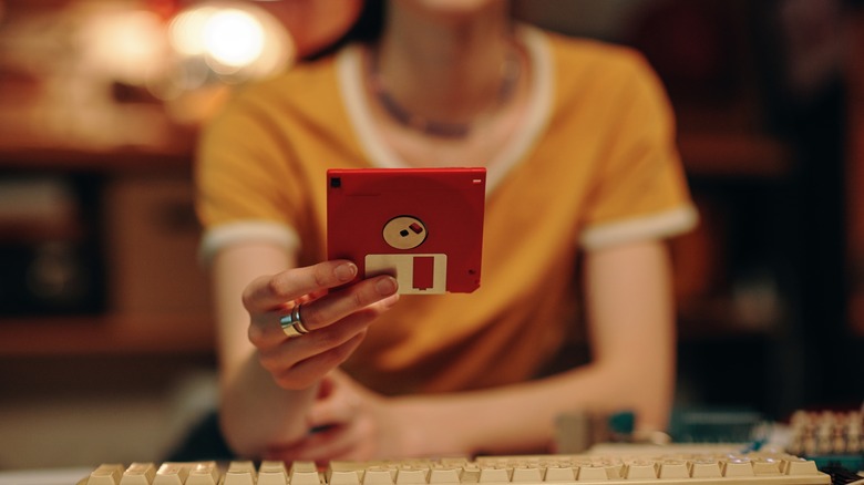 A person holding a red floppy disk above a keyboard