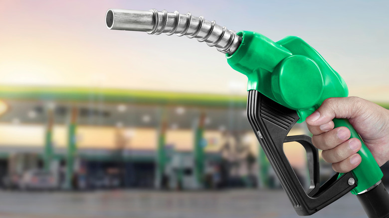 Person holding gas pump in front of an out-of-focus gas station