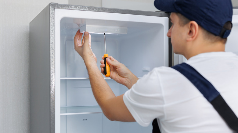 Man in a uniform repairs the light in the refrigerator