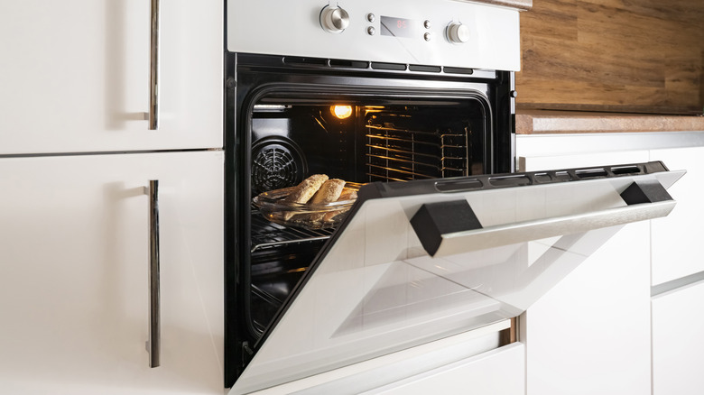 A wall oven in white with door ajar showing interior light bulb