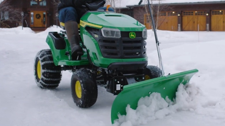 A person plowing snow with a John Deere riding mower, close-up shot