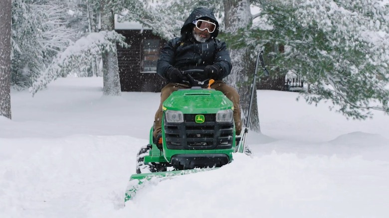 A person plowing snow on a John Deere mower.
