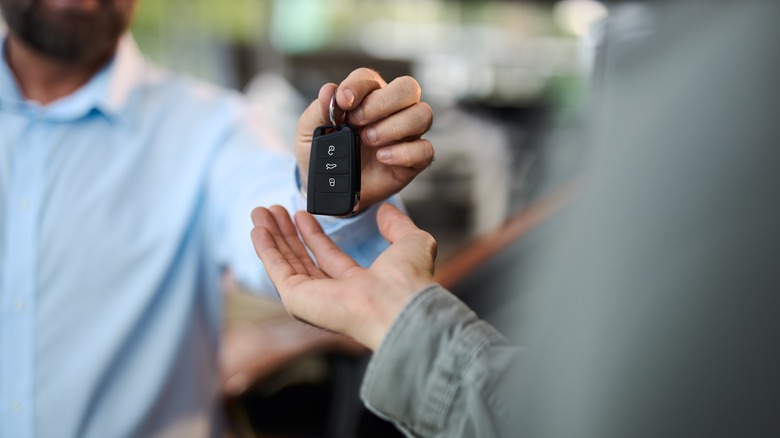 Car salesman handing car keys to customer in a showroom