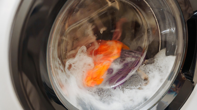 A close-up of a front-load washing machine mid-cycle with soap and orange clothing visible