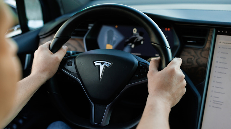 A person behind the wheel of a Tesla holding both hands on the steering wheel.