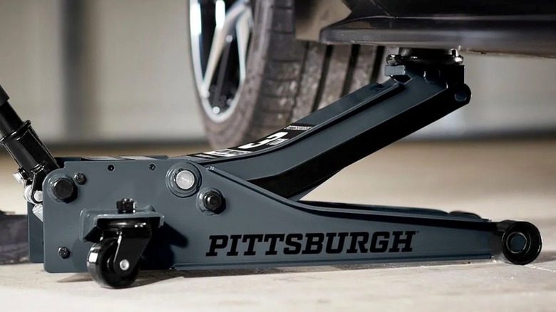 The Pittsburgh 3-Ton Low-Profile Floor Jack from Harbor Freight, a highly-rated budget-friendly floor jack, is being used to lift a car.