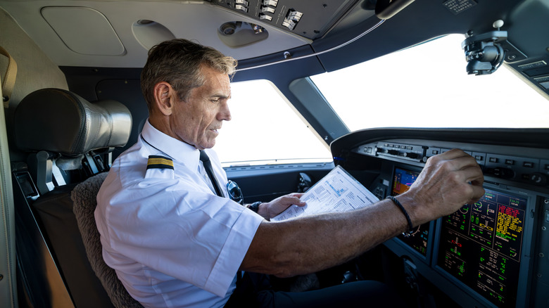 older male pilot adjusting radio controls in plane cockpit