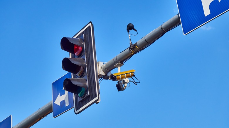 A red traffic light surrounded with sensors, cameras, and traffic signs.
