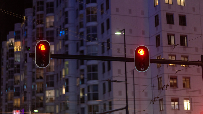 Two red traffic lights in the dark with a large building in the background.