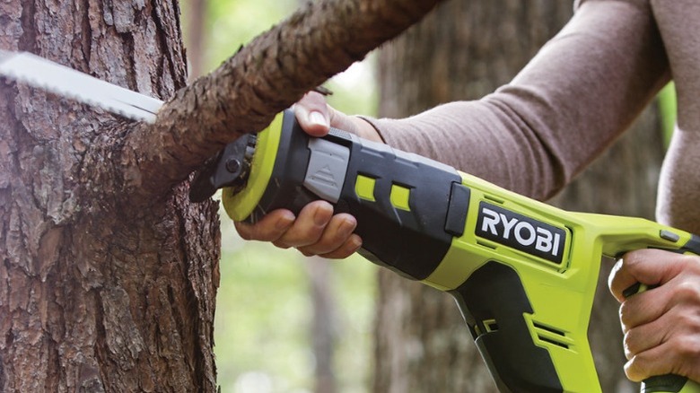 Person cutting tree limb with Ryobi reciprocating saw