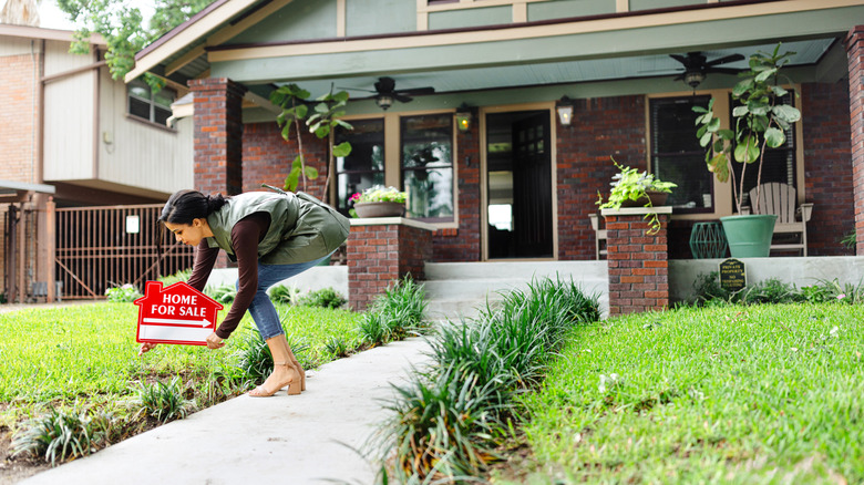 Woman placing home for sale sign in yard