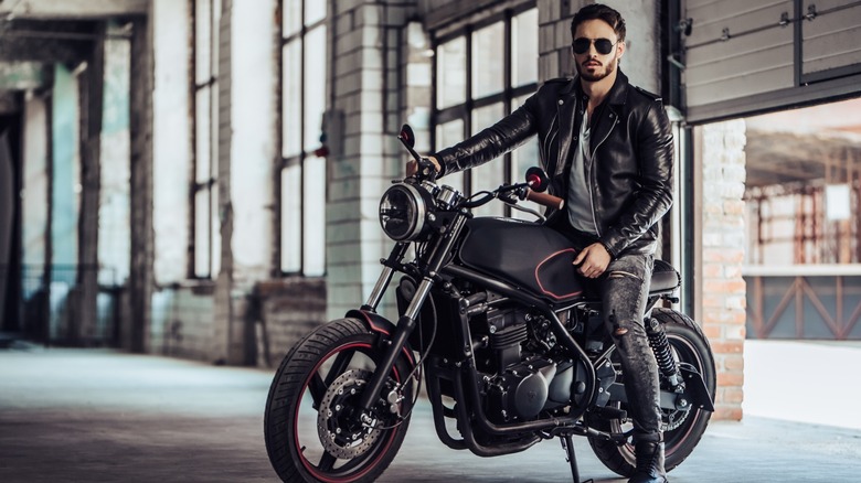 A person posing with a black motorcycle in a warehouse