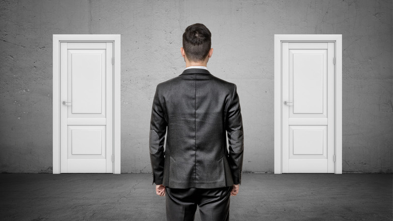 A man in a suit facing two identical white doors.