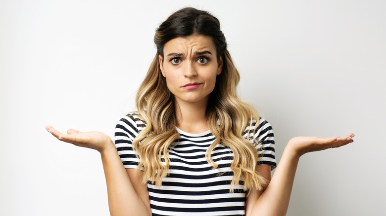 A woman with long blonde hair, a stripy shirt, and a puzzled expression.