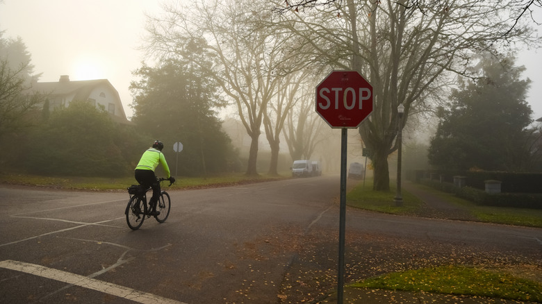 A man in a bright yellow jacket on a bicycle cruising through an intersection with a stop sign in a residential area