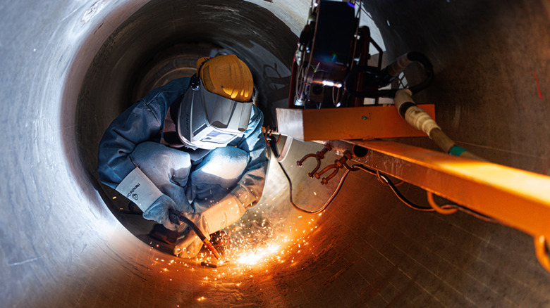Worker in mask welding large metal tube during submarine construction