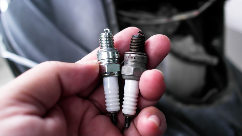 Left hand holding new and used spark plugs together
