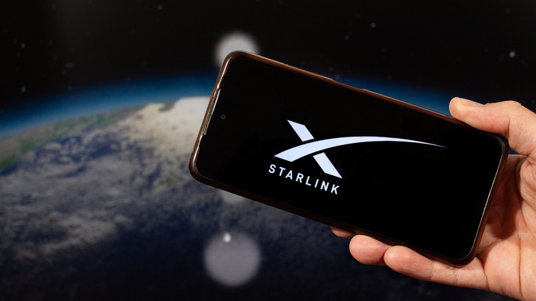 A hand holding a smart phone with the Starlink logo displayed with the planet Earth in the background,