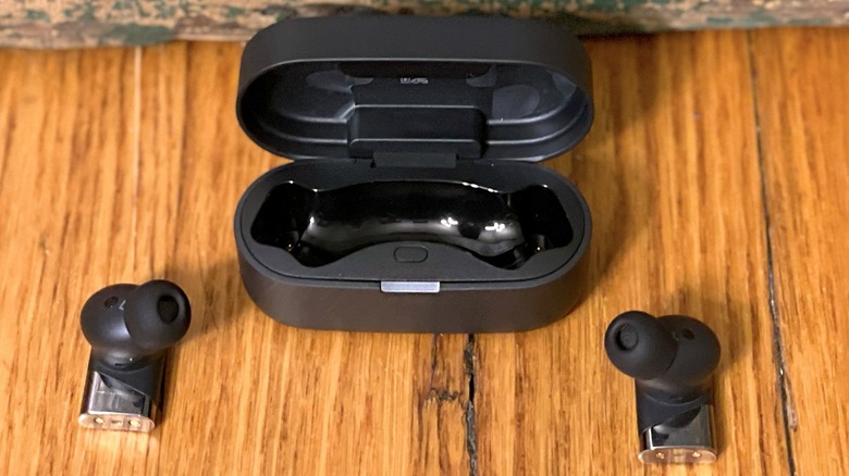 Person with glasses looking at a smartphone while wearing Status Pro X earbuds.