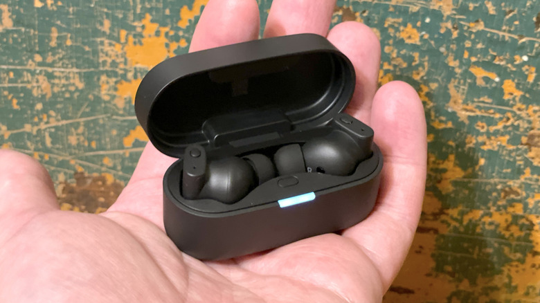 Hand holding an open Status Pro X charging case with the earbuds inside.