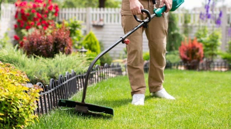 a person using a string trimmer to edge around a flower bed