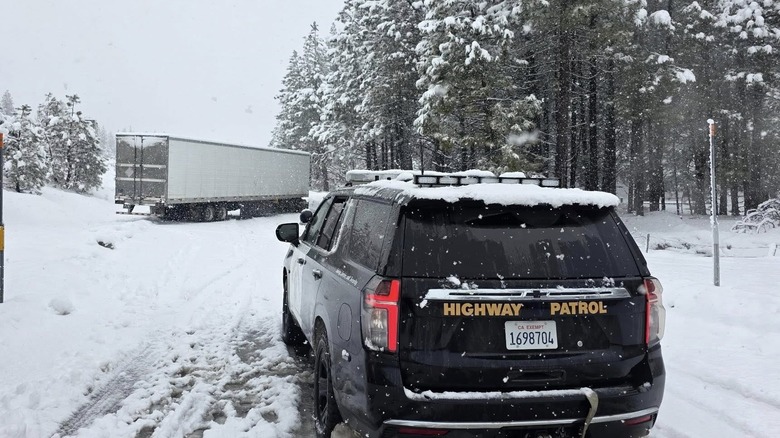 California Highway Patrol vehicle facing stuck semi-truck in snow