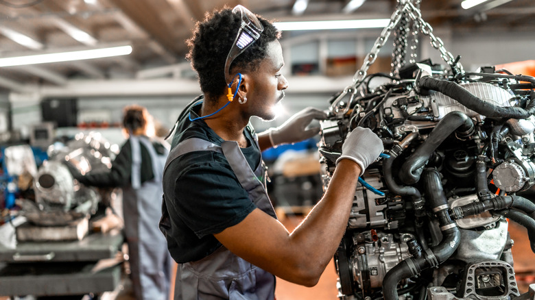 Young mechanic repairing a car engine hanging from a chain hoist