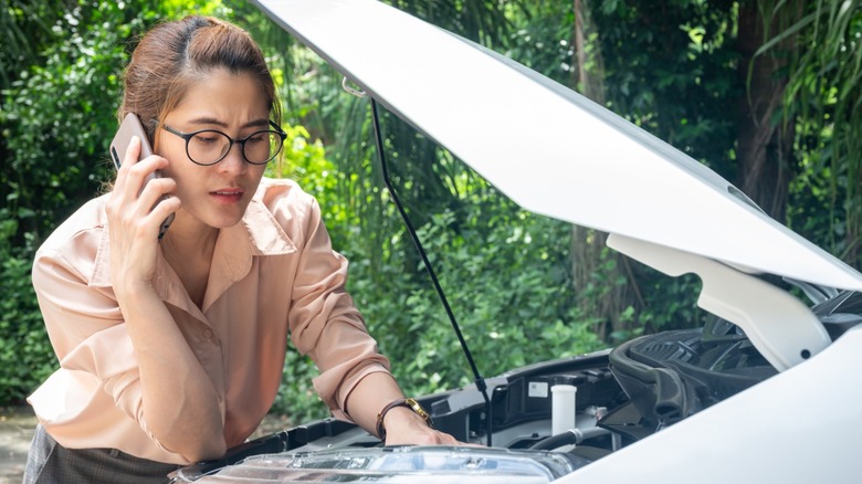 Woman making a phone call with a car hood open