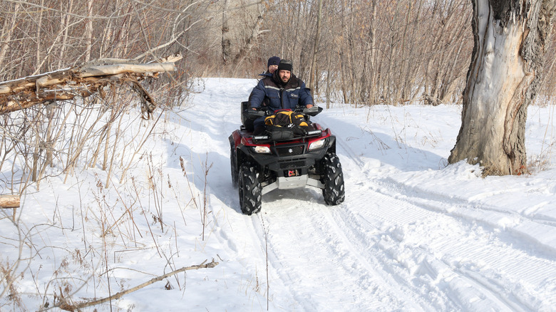 Two people driving ATV on snowy path in forest