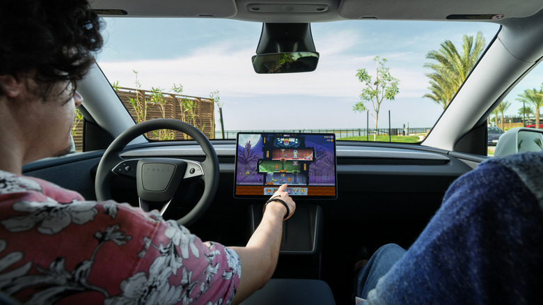Interior view of a Tesla Model Y driver interacting with the touchscreen while parked