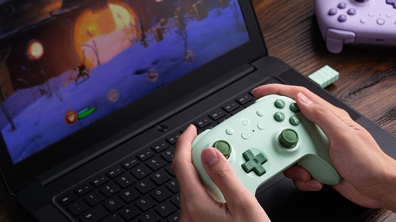 A person playing a game on a laptop using a controller
