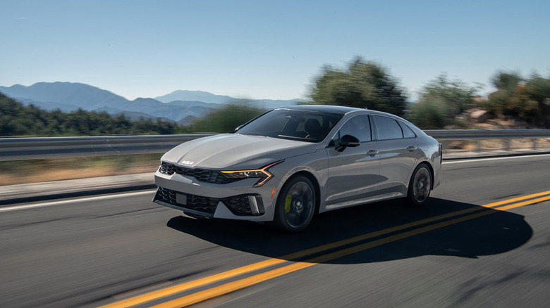 A silver Kia K5 driving along a highway
