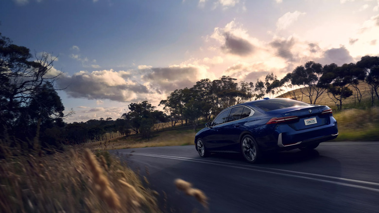 A blue BMW 5-series sedan driving on a country road