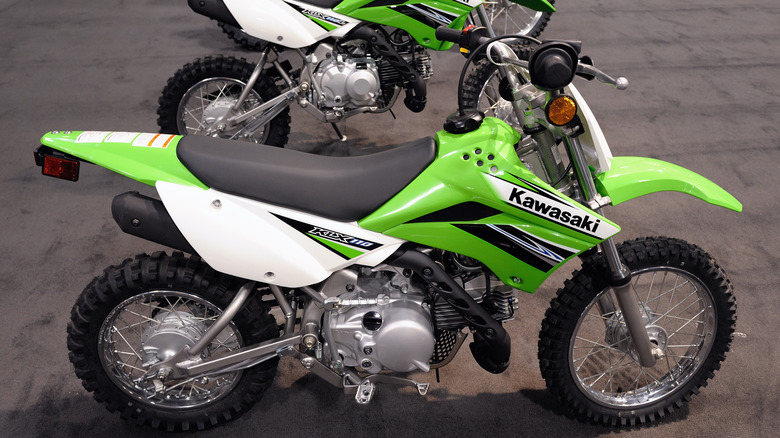 A bright green Kawasaki KLX 110 modelparked alongside another one in the back.