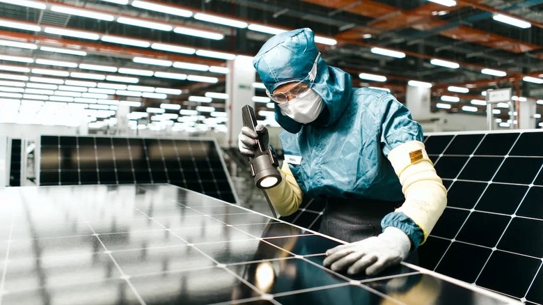 A worker wearing a clean-suit inspects the fine details of a solar panel.