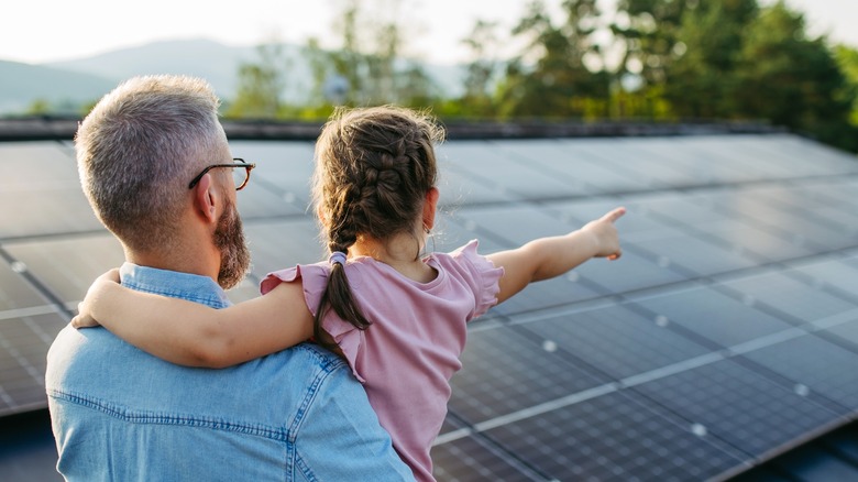 A man holding a young girl while looking at installed solar panels.