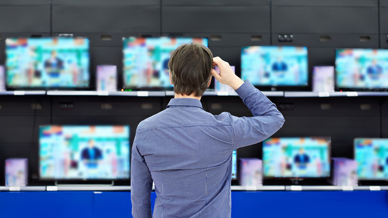 man looks at televisions