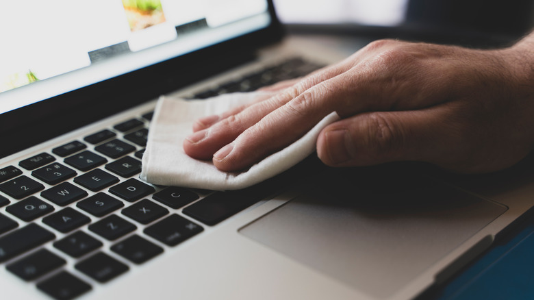 A hand wiping laptop keyboard with cloth