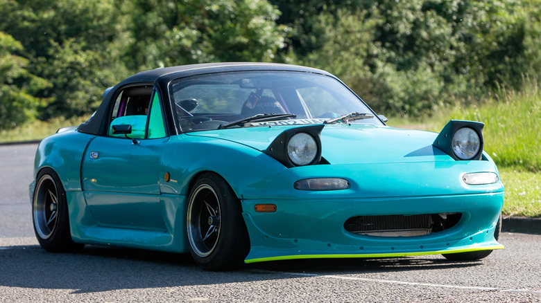 1992 Blue Mazda Miata MX-5 with pop-up headlights riding on a British country road