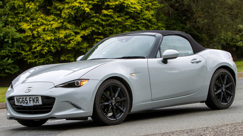 A 2016 silver Mazda Miata cruising on an English country road