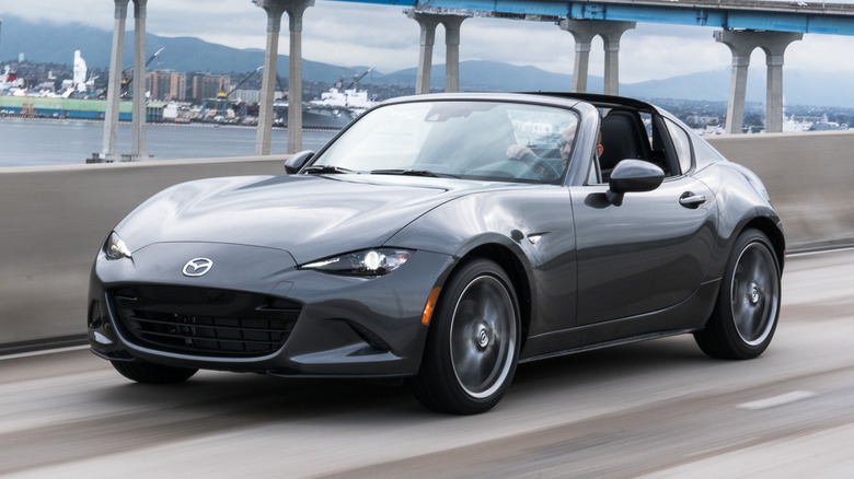 A 2018 Mazda Miata RF in silver color cruising in the road with a bridge in the background